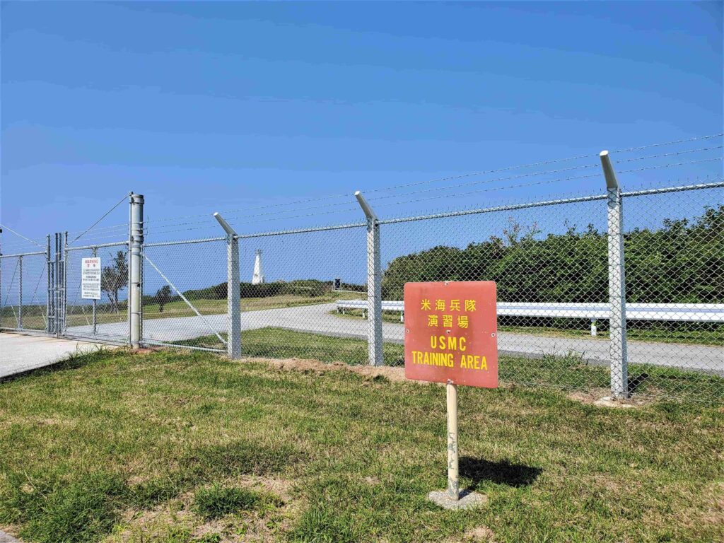 米軍演習場の看板と金網の向こうに建つ伊江島灯台