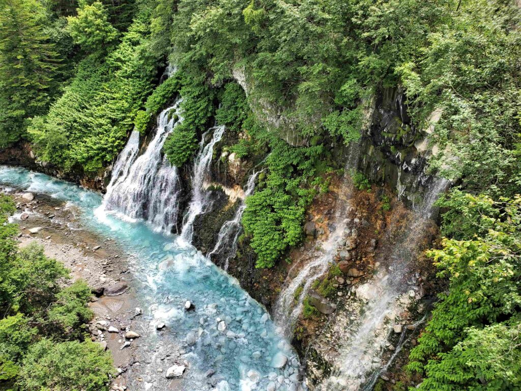 緑に囲まれた岩の間から水が川に流れ出る白ひげの滝の風景